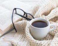 Buch, Kaffee und schwarze Brille auf liegen auf warmem Cardigan