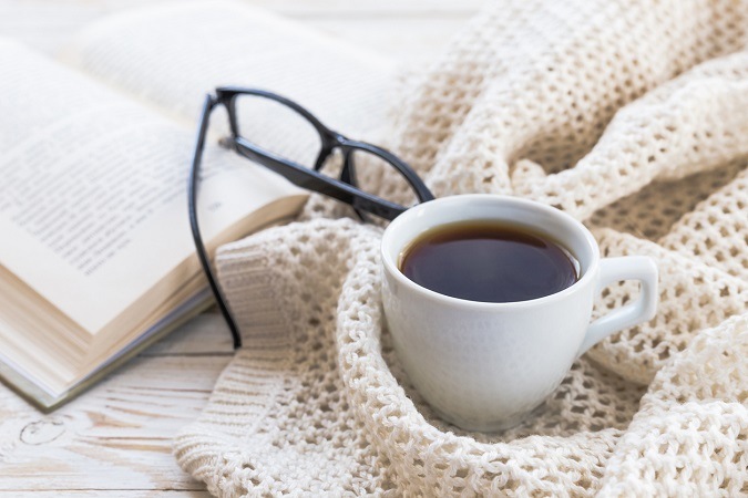 Buch, Kaffee und schwarze Brille auf liegen auf warmem Cardigan