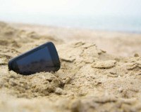 Ein Handy liegt am Strand im Sand.