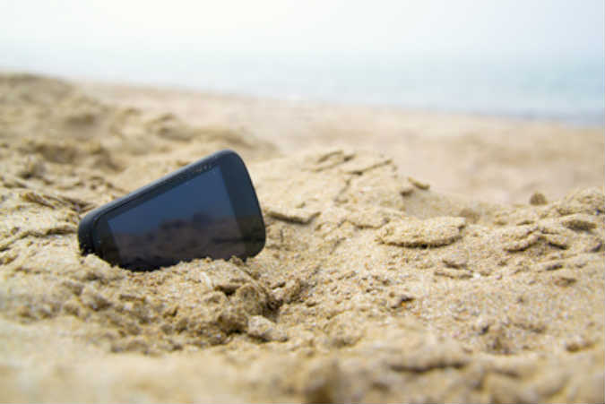 Ein Handy liegt am Strand im Sand.