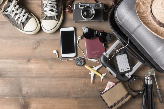 Reiseutensielien liegen neben dem Koffer für den Sommerurlaub