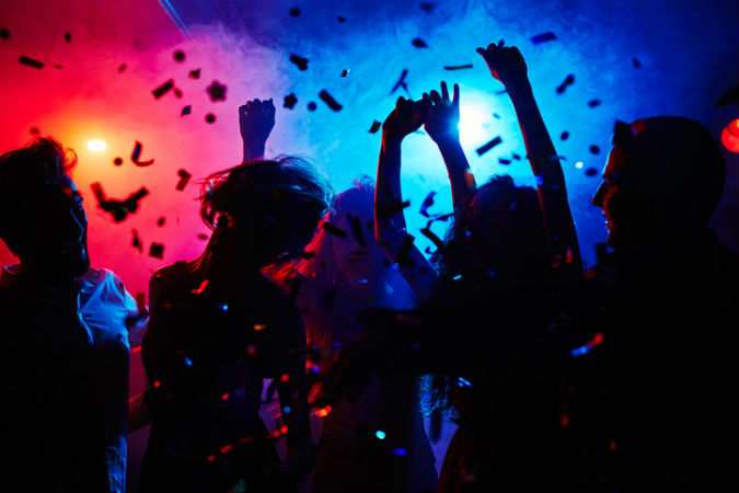 Menschen tanzen im Club in buntem Nebellicht und Konfetti