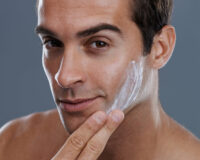 Studio shot of a handsome young man applying cream to his face