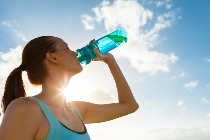 Frau trinkt aus Sportflasche, Himmel im Hintergrund