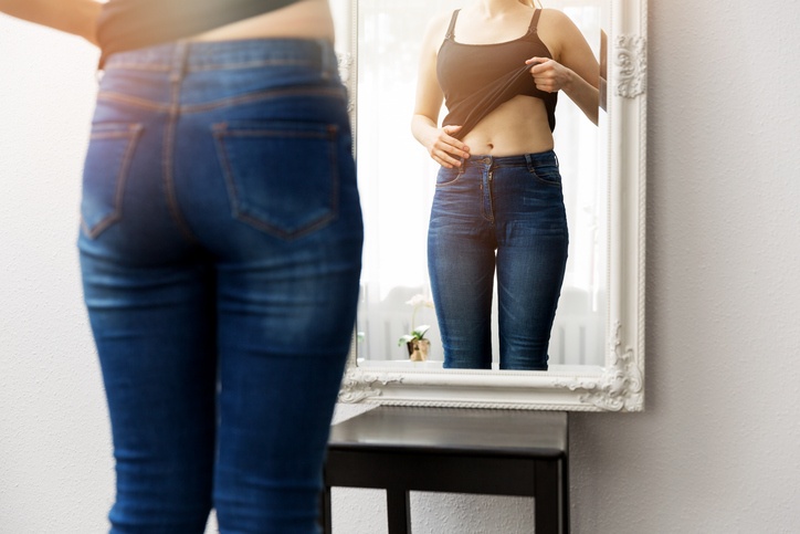 Frau kontrolliert ihren Körper vor dem Spiegel