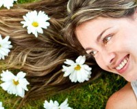 Frau mit lange blonden Haaren liegt mit dem Rücken im Gras und hat Blumen im Haar
