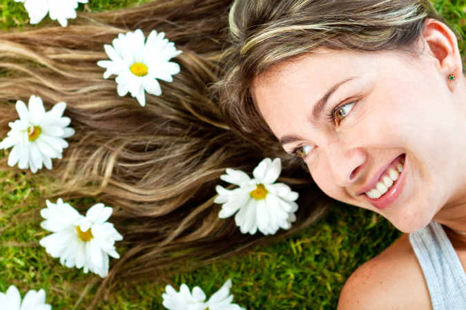 Frau mit lange blonden Haaren liegt mit dem Rücken im Gras und hat Blumen im Haar