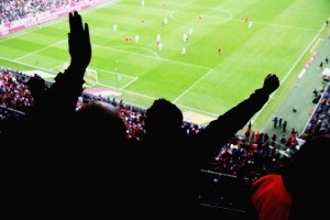 Blick von der Tribüne des Stadions auf das Spielfeld mit jubelnden Fans auf den Rängen