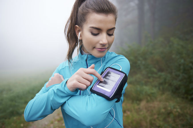 Junge Frau beim Joggen im Wald mit mobiler Fitness-App